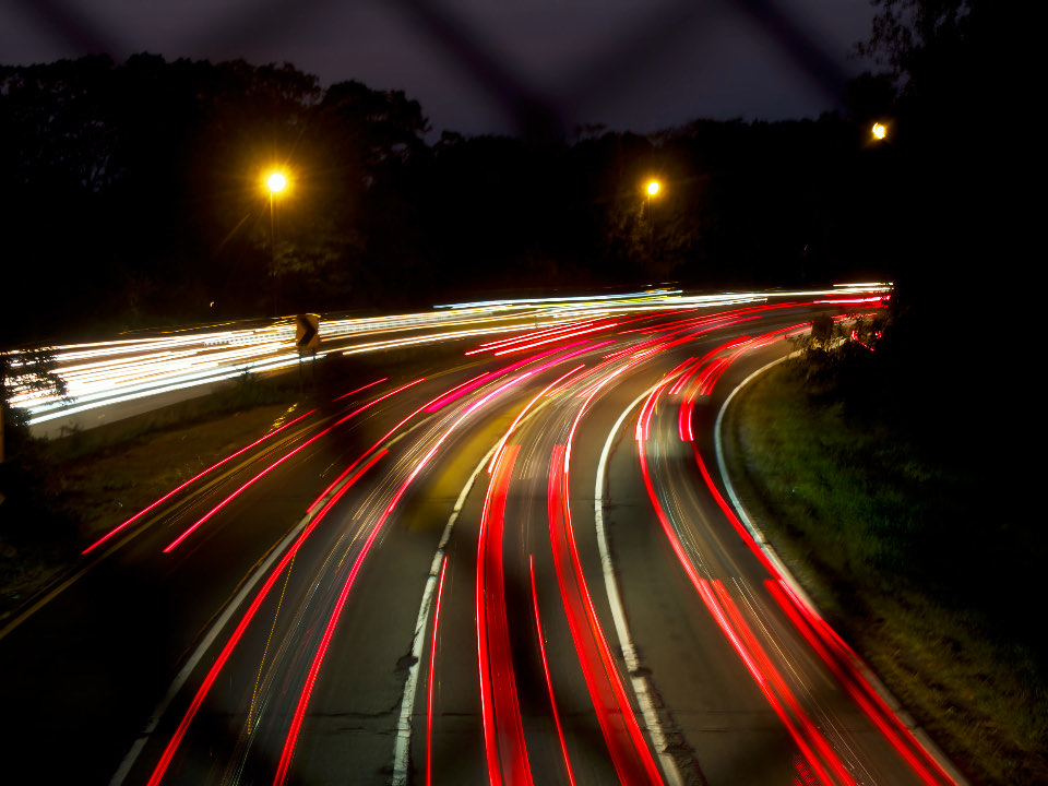 Traînées lumineuses de voitures la nuit sur une route sinueuse
